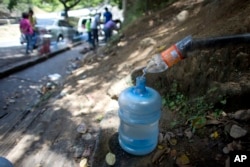A water bottle is used as a funnel to fill a large container with water trickling from a hillside spring, during water shortages in Caracas, Venezuela, June 14, 2018.