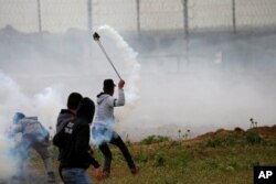 A Palestinian demonstrator uses a sling to hurl back a tear gas canister fired by Israeli forces during a protest marking Land Day and the first anniversary of a surge of border protests, at the Israel-Gaza border fence east of Gaza City, March 30, 2019.