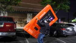 FILE - A masked shopper leaves a Walmart store with a TV in Pic Rivera Calif., Nov. 26, 2021. From appliance stores in the United States to food markets in Hungary and gas stations in Poland, rising consumer prices fueled by high energy costs and supply chain disruptions are putting a pinch on households and businesses worldwide.