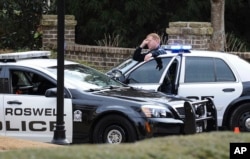 FILE - Roswell Police officers stand guard next to his patrol car in Roswell, Ga., Saturday, Jan. 31, 2015.