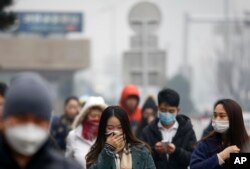 FILE - A woman uses a scarf and others wear masks to cover their face from pollutants as they walk along a street on a polluted day in Beijing.