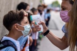 FILE - A teacher wearing a face mask to protect against the spread of coronavirus checks the temperature of her student at Maestro Padilla school as the new school year begins, in Madrid, Sept. 7, 2021. (AP)