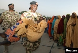 FILE - Major General Rogers Nicholas carries one of the newly released Dapchi schoolgirls as others wait to board a plane in Maiduguri, Nigeria, March 21, 2018.