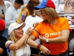Mariana Anillo, left, of Venezuela helps fellow Venezuelan Rita Sanchez put on a blue ribbon as they watch televised news from their country at the El Arepazo Doral Venezuelan restaurant in Doral, Fla., April 30, 2019.