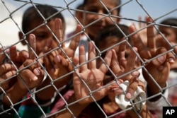FILE - Syrian refugee children wave and flash the V-sign at a refugee camp in Suruc, on the Turkey-Syria border, June 19, 2015.