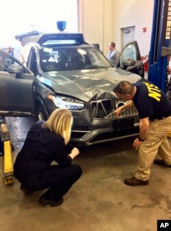 FILE - In this March 20, 2018, file photo provided by the National Transportation Safety Board, investigators examine a driverless Uber SUV that fatally struck a woman in Tempe, Ariz.