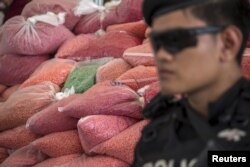 FILE - A police officer from the Narcotics Control Board guards bags of methamphetamine pills during a Destruction of Confiscated Narcotics ceremony in Ayutthaya province, north of Bangkok, Thailand. The significant organized crime threat involves not only narcotics but also human trafficking and wildlife smuggling.