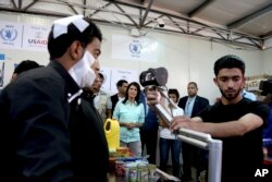 U.S. Ambassador to the United Nations Nikki Haley, background center, looks on as a bandaged Syrian refugee has his iris scanned at a supermarket, May 21, 2017, in Zaatari Refugee Camp, Jordan.