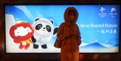 A woman waits on a bus station in front of an advertising board featuring Bing Dwen Dwen, the Beijing 2022 Winter Olympic Mascot and Shuey Rhon Rhon, the 2022 Beijing Winter Paralympic Games Mascot, in Beijing on January 19, 2022. (Fabrizio Bensch/Reuters)