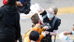 Žena poliva mlekom lice demonstranta koga je policija isprskala suzavcem drugog dana protesta u Mineapolisu.