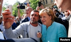 FILE - A migrant takes a selfie with German Chancellor Angela Merkel outside a refugee camp near the Federal Office for Migration and Refugees after registration at Berlin's Spandau district, Germany, Sept. 10, 2015.