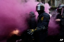 FILE - Catalan Mossos d'Esquadra regional police officers stand amid smoke from a smoke bomb during clashes with pro-independence supporters trying to reach the Spanish government office in Barcelona, Spain, March 25, 2018.