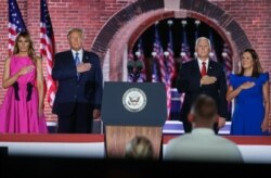 U.S. President Donald Trump, first lady Melania Trump, U.S. Vice President Mike Pence and his wife Karen Pence hold their hands over their hearts as they listen to singer Trace Atkins sing the U.S. National Anthem after Pence's acceptance speech as the 20