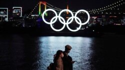 A man and a woman walk past near the Olympic rings floating in the water in the Odaiba section Tuesday, Dec. 1, 2020, in Tokyo.