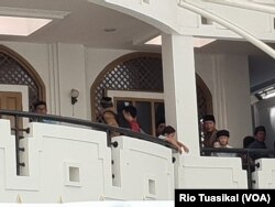 Peserta diskusi buku "Haqiqatul Wahy" dari Ahmadiyah dan masyarakat umum melihat situasi dari beranda masjid di tengah-tengah orasi untuk penghentian acara sesuai negosiasi. (Foto: VOA/Rio Tuasikal)