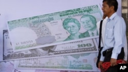 បុរស​ខ្មែរ​ម្នាក់​ឈរ​នៅ​ក្មេង​ផ្លាក​លុយ​រៀល​របស់​កម្ពុជា​ក្នុង​ពិធី​សម្ភោធ​ផ្សារ​លក់​ភាគ​ហ៊ុន​របស់​កម្ពុជា នៅ​រាជធានី​ភ្នំពេញ កាល​ពី​ថ្ងៃ​ច័ន្ទ ទី១១ ខែ​កក្កដា ឆ្នាំ២០១១។ (រូប​ថត​ដោយ៖ AP)