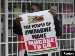FILE - A man carries a poster calling for Zimbabwe President Robert Mugabe to step down as Zimbabweans take to the streets in Harare, Zimbabwe, Nov. 18, 2017.
