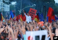 Lulzim Basha, leader of the main opposition Democratic Party, standing in background, flashes the victory sign during an anti-government protest in Tirana, Albania, June 8, 2019.