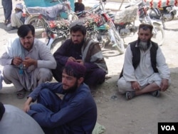Afghans waiting to return home sit in the shade of the customs office wall, Aug. 24, 2016. (Photo: A. Khan/VOA)