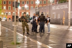 Police officers and a soldier stand by the sealed off area of an attack after a truck drove on to the sidewalk and plowed through a crowd of revelers who'd gathered to watch the fireworks in the resort city of Nice, southern France, July 15, 2016.