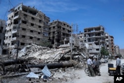 People stand in front of damaged buildings, in the town of Douma, the site of a suspected chemical weapons attack, near Damascus, Syria, April 16, 2018.