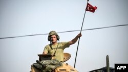 FILE - A soldier gestures as Turkish Army tanks drive to the Syrian-Turkish border town of Jarablus, Aug. 25, 2016
