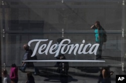 People are reflected in a glass sign of a Telefonica building in Madrid, Spain, May 13, 2017. The Spanish government said several companies including Telefonica had been targeted in ransomware cyberattack that affected the Windows operating system of employees' computers.