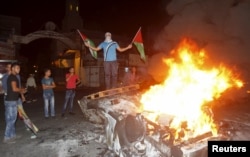 A Palestinian holding Palestinian flags stands on a burning car belonging to Jewish settlers after it was set on fire by Palestinians in the West Bank city of Nablus, Oct. 18, 2015.