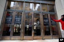 A woman waves from the sidewalk as another locks the front door at Lord & Taylor's Fifth Avenue flagship store which closed for good mid-afternoon, Jan. 2, 2019, in New York.