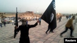 FILE - A fighter of the Islamic State group holds an IS flag and a weapon on a street in the city of Mosul, Iraq, June 23, 2014.