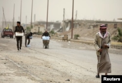 A civilian and fighters from the Syrian Democratic Forces (SDF) walk along a street in the Raqqa's al-Sana'a industrial neighborhood, Syria June 14, 2017.