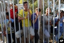 Central American migrants peer out from a shelter as anti-migrant demonstrators protest their presence one block away, in Tijuana, Mexico, Nov. 18, 2018.