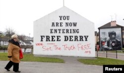 FILE - A woman walks past murals in Bogside, Derry, Northern Ireland, March 23, 2010.