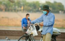 អាជីករលក់ចំណីអាហារម្នាក់ដែលមានពាក់ម៉ាស់ ដើរលក់នៅសួនក្បែរព្រះបរមរាជវាំង ខណៈ​កម្ពុជា​កំពុង​ប្រឈម​ការ​រាតត្បាត​នៃ​ជំងឺកូវីដ១៩​ នៅ​ភ្នំពេញ ថ្ងៃទី១០ ខែមីនា​ ឆ្នាំ២០២១។​ (ហ៊ាន​ សុជាតា/វីអូអេ)