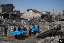 FILE - Residents carry the body of several people killed during fights between Iraq security forces and Islamic State on the western side of Mosul, Iraq, March 24, 2017.