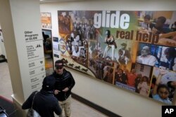 In this Feb. 12, 2019 photo, people walk past a display and directory to the many assistance programs at the Glide Memorial United Methodist Church in San Francisco.