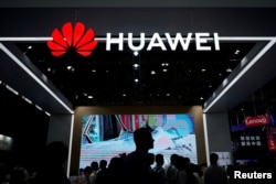 FILE - People walk past a sign board of Huawei at CES (Consumer Electronics Show) Asia 2018 in Shanghai, China, June 14, 2018.