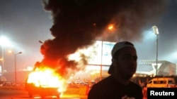 A soccer fan is seen near a police car, which was set on fire by fireworks, during clashes between soccer fans and security forces in front of a stadium on the outskirts of Cairo February 8, 2015.