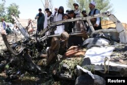 Afghan men inspect a car damaged in a suicide car bomb attack in Khost province, May 27, 2017.
