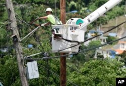 FILE - A worker from the Cobra Energy Co., contracted by the Army Corps of Engineers, installs power lines in the Barrio Martorel area of Yabucoa, a town where many residents continue without power in Puerto Rico, May 16, 2018.