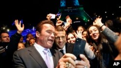 Arnold Schwarzenegger, à côté du président français Emmanuel Macron, au centre, prennent un selfie avec des jeunes devant la Tour Eiffel illuminée en vert, à bord d'un bateau qui navigue sur la Seine depuis le One Planet Summit, mardi 12 décembre 2017