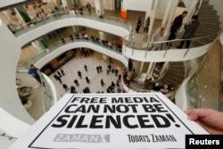 FILE – A journalist holds a banner at the headquarters of Zaman daily newspaper in Istanbul on Dec. 14, 2014, after Turkish police raided a television station and newspaper.