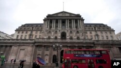 FILE - People hold umbrellas to shelter from the rain as they walk past the Bank of England in London, Aug. 4, 2011.