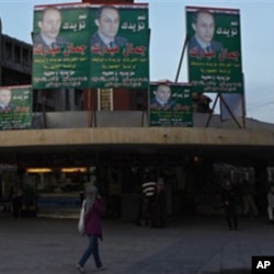 An Egyptian woman walks under electoral posters supporting the ruling National Party with a picture of Gamal Mubarak, son of President Hosni Mubarak, in Alexandria, 27 Nov 2010