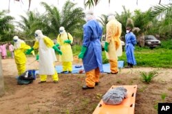 FILE - The wrapped remains of a new born child suspected of contracting the Ebola virus, lays on a stretcher as health workers, dressed in Ebola protective gear, move the body for burial in Dubreka, Guinea, June 19, 2015.