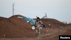 A rebel fighter from Jaysh al-Sunna carries food as he walks along a sand barricade in Tel Mamo village, in the southern countryside of Aleppo, Syria, March 13, 2016.