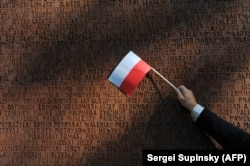A person waves a Polish flag at a monument dedicated to Polish officers murdered in the 1940 Soviet-era Katyn massacre, near Kharkiv, Ukraine.