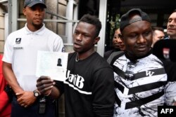 Malian migrant Mamoudou Gassama (C) flanked by his older brother (R) holds his temporary residence permit after receiving it at the Prefecture of Bobigny, northeast of Paris, on May 29, 2018.