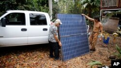 Edwin Montoya, left, and Abe Pedro, load a solar panel removed from the Montoya family's property onto a truck, May 18, 2018, near Pahoa, Hawaii. Montoya family owns a farm near Pohoiki Road and lava crossed the road near his property, Friday, blocking access to the neighborhood.