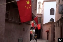 In this Nov. 4, 2017, photo, a child reacts to a stranger as adults chat along the corridor of the old city district where Chinese national flags are prominently hung in Kashgar in western China's Xinjiang region.